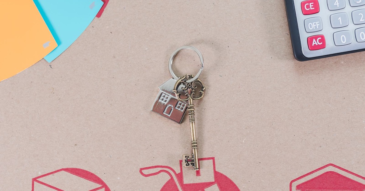 House-shaped keyring and key on a moving box beside a calculator and property-planning papers.